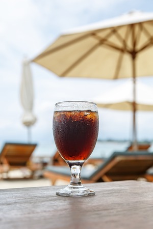 Cola glass on beach with umbrellas. Cooling drink on summer.の写真素材