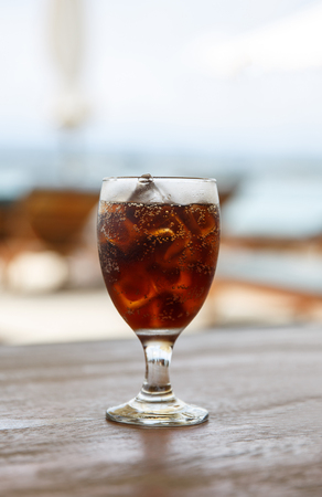 Tulip glass with cola on table. Beach umbrellas on the backgroundの写真素材