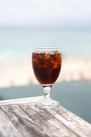 Tulip glass with cola on table. Beach umbrellas on the backgroundの写真素材