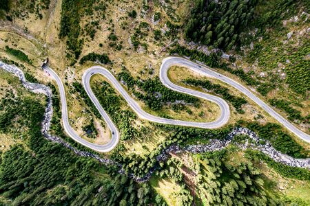 Winding road with a lot of turns, top view. Mountain river nearbyの写真素材