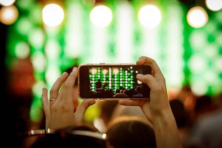 Mobile phone in hand during the shooting of a concert, light showの写真素材