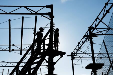 Little boy and girl walk on adventure rope park. Black silhouetteの写真素材