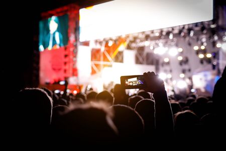 Silhouette of people with smartphones in hands at a music concert in front of stage lightsの写真素材