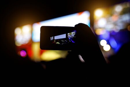 Silhouette of people with smartphones in hands at a music concert in front of stage lightsの写真素材