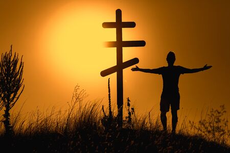 Silhouette of man near orthodox cross on the background of the sunset.の写真素材