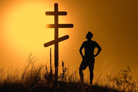 Silhouette of man near orthodox cross on the background of the sunset.の写真素材