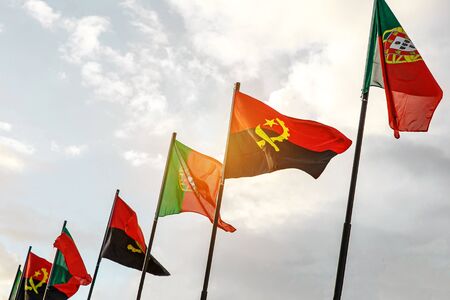 Row of Portugal and Angola flags waving in the wind against white cloudy blue sky together. Diplomacy concept, international relations.の写真素材