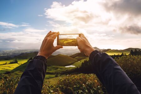 Man takes a photo of a beautiful green meadow on his smartphone.の写真素材
