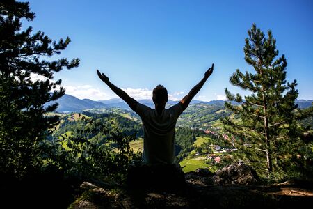 Happy Man raised hands in front of a beautiful green valley in the mountains. Travel lifestyle emotional conceptの写真素材