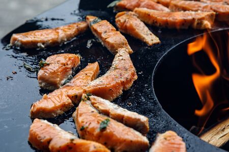Grilled salmon fish with various vegetables and spices on pan near the fireの写真素材
