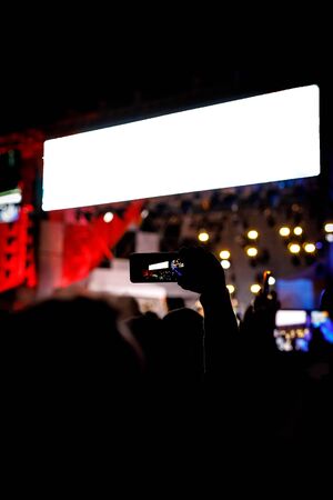 Silhouette of hands with a smartphone at a big music festival, video recording of stage showの写真素材