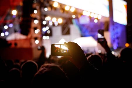 Silhouette of people holding their smart phones and photographing concertの写真素材