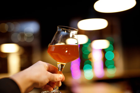 Beer glass with a thin leg in hand. Blurry bar background
