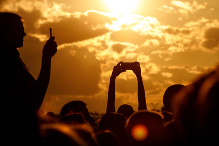 Silhouette of hand using smartphone to take pictures and videos at outdoor music show