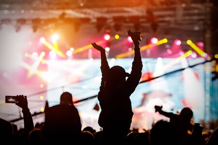 The crowd with their hands up enjoys music concert. Fan silhouette on stage backgroundの写真素材