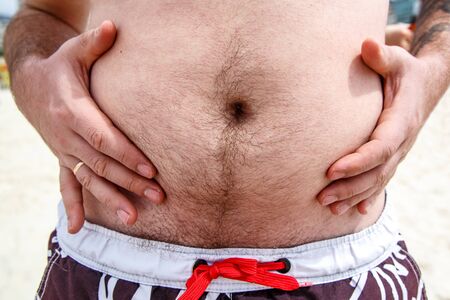 Close up of an obese fat man showing his belly on the beachの写真素材