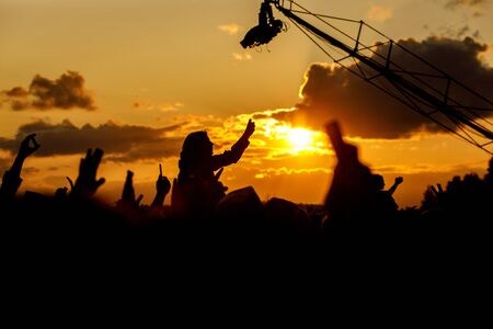 Girl over the crowd against the sunset sky. Having fun and using her smartphone at the summer festival.の写真素材