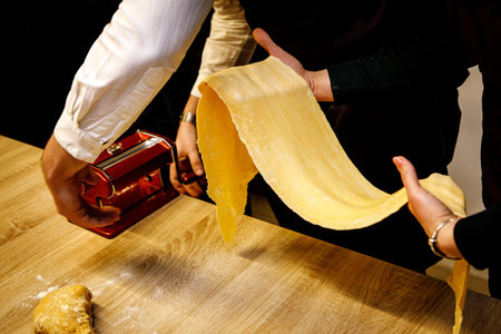 Noodles and pasta machine and long piece of dough in hands