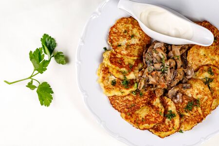Potato pancakes with mushrooms and sour cream on a white plate.の写真素材