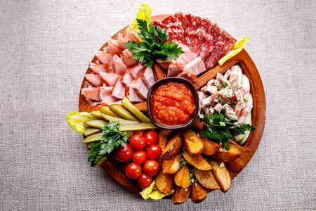 Round wooden tray with different snacks. Ham, vegetables, pickles, cherry tomatoes and sauce in the centerの写真素材