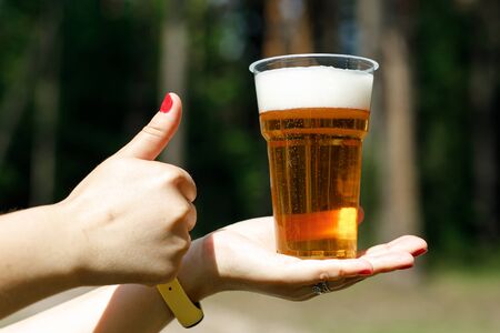 The girl holds a disposable plastic cup with beerの写真素材