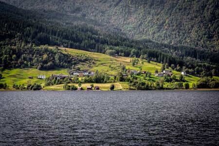 Traditional Norwegian houses near the lake with green forest on mountains on background.の写真素材