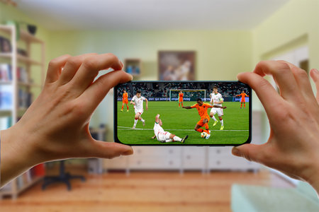 Minsk. Belarus - 20.04.2020: Watching football game at home via smartphone. Broadcasting soccer from the stadiumのeditorial素材