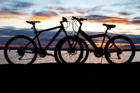 Black silhouette of a bicycle at sunset on the beach near the lakeの写真素材