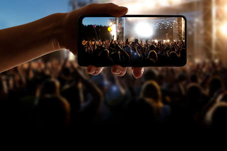 Silhouette of hand using camera phone to take pictures and videos at pop concert, festival.の写真素材