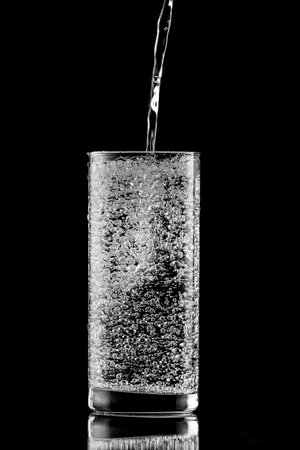 Pouring water into a glass on a black backgroundの写真素材
