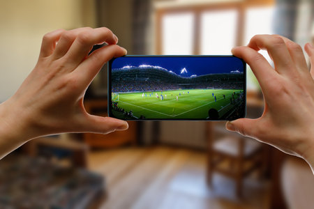 Watching football game at home via smartphone. Broadcasting soccer from the stadiumの写真素材