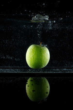 Green apple splashing into water on black background.の写真素材