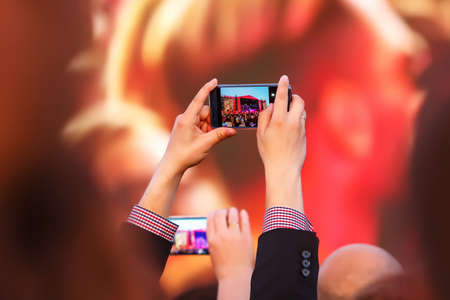 Taking a photo by mobile phone at a concert in front of the stage lightの写真素材