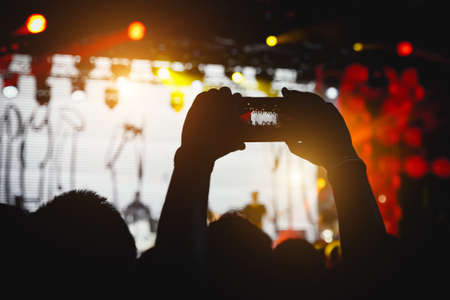 Man takes a picture of the show at the concert hall using a smartphoneの写真素材