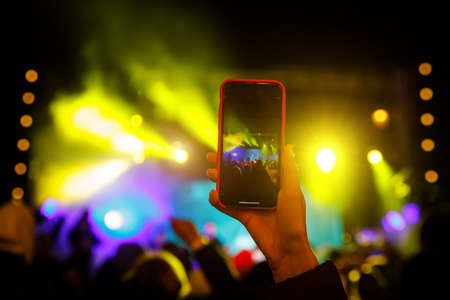 Using a smartphone in a public event. Holding a mobile phone in hands and shooting photo or video contentの写真素材