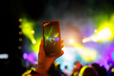Using a smartphone in a public event. Holding a mobile phone in hands and shooting photo or video contentの写真素材