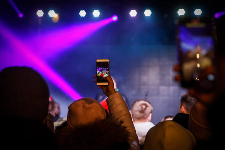 Using a smartphone in a public event. Holding a mobile phone in hands and shooting photo or video contentの写真素材