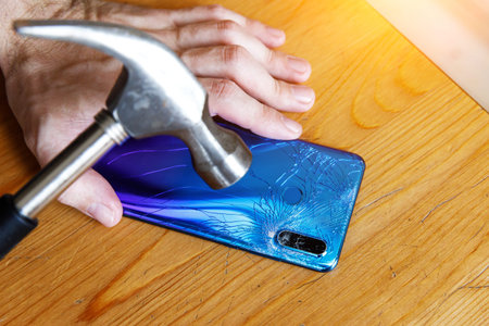 Broken smartphone camera and hammer on wooden background