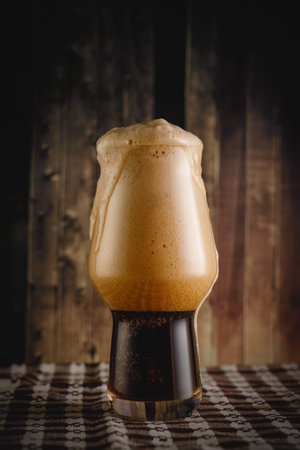 A glass of dark beer on wooden table.