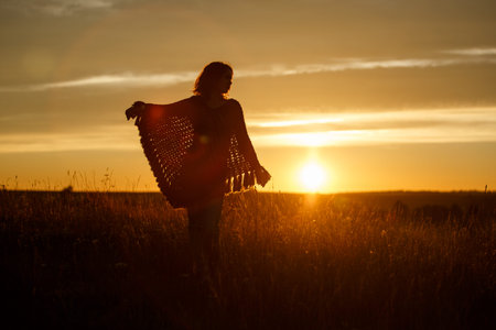 silhouette of happy young woman on sunset, outdoor girl in a plaid poncho in a field with spikeletsの写真素材
