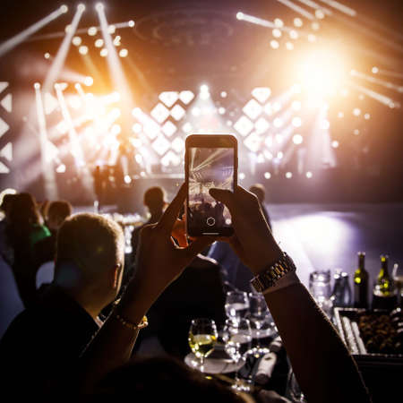 Hands with a smartphone at the concert hall during music and light showの写真素材