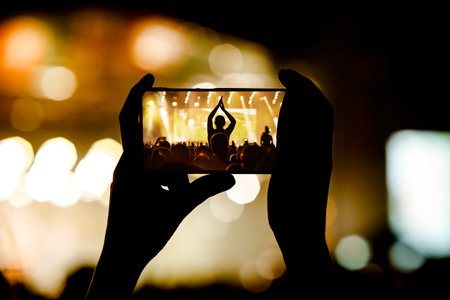 Hand with a smartphone records live music festival and taking photo of concertの写真素材