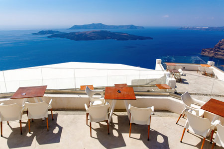 Empty restaurant tables on a sunny terrace in Santorini. Sea and caldera in the backgroundの写真素材