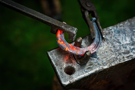 Horseshoe production process. A blacksmith bending hot metal on an anvilの写真素材