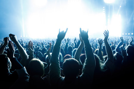 Performance of a popular group. The crowd with raised hands against the stage lightの写真素材
