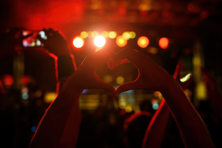 A person is making a heart sign during a concert of a favorite music band. Black silhouette