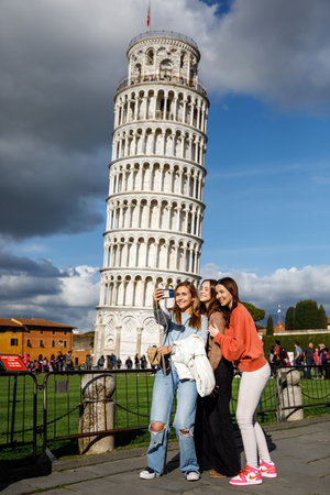 Pisa, Italy - March 27, 2023: Three happy girls, friends taking a selfie on famous leaning tower backgroundのeditorial素材