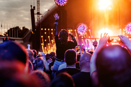 Stage lights against a happy woman with raised arms while enjoying a concert at a music festival.の写真素材