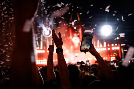 Happy people on the dance floor record a big music concert using a mobile phone. Confetti over...