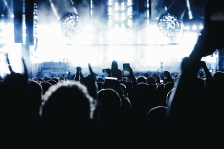 Performance of a popular group. The crowd with raised hands against the stage light.